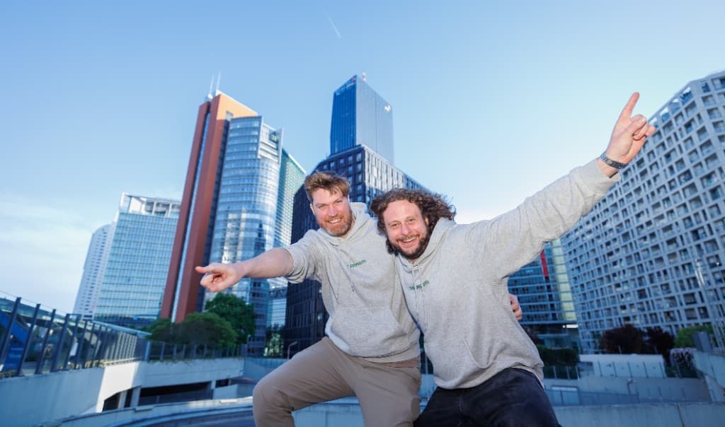 Ole-André Riga-Johansen and Jens Skaaland in Happypath hoodies, arms stretched out, in front of glass office towers